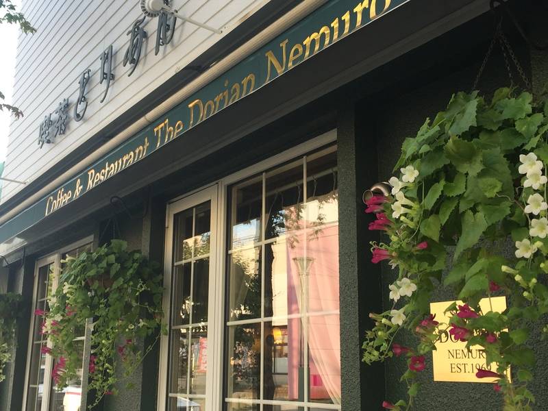 「Coffee & Restaurant The Dorian Nemuro」の看板と吊り鉢の花が飾られたどりあんの緑の店構え