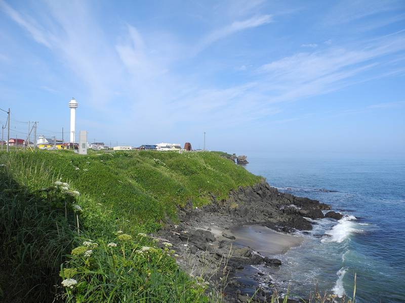 納沙布岬の白い灯台と、草におおわれた崖と岩の海岸